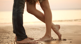 A loving young couple hugging and kissing on the beach. Lovers man and woman barefoot in the wet sand. Summer in love.