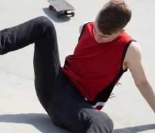 Young man fall off  skate board, sitting on concrete ramp.