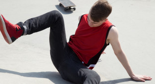 Young man fall off  skate board, sitting on concrete ramp.