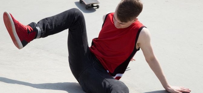 Young man fall off  skate board, sitting on concrete ramp.