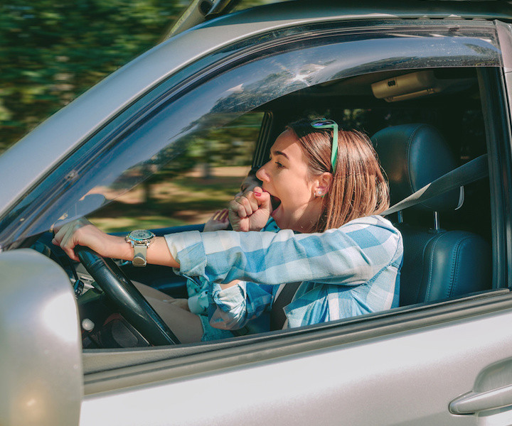 Tired young woman driving car and yawning