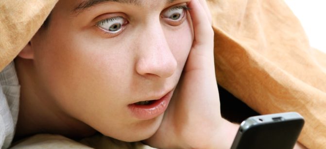 Surprised Teenager with Cellphone under Blanket at the Home