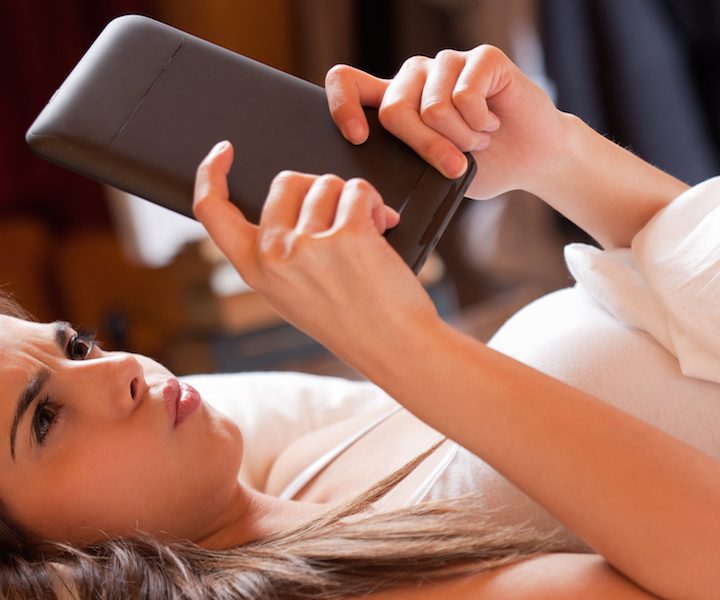 Cute young brunette  using tablet computer laying in bed.