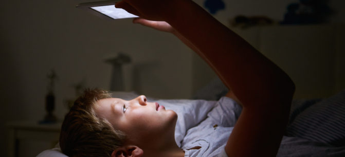Boy Looking At Digital Tablet In Bed At Night