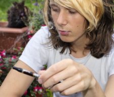 A teenage boy sitting in a garden, smoking an electronic cigarette and exhaling vapour