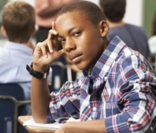 Bored Male Teenage Pupil In Classroom Looking At Camera Leaning On Arm