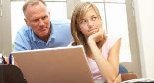 Angry Father And Teenage Daughter Using Laptop At Home