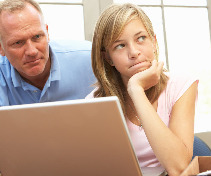 Angry Father And Teenage Daughter Using Laptop At Home
