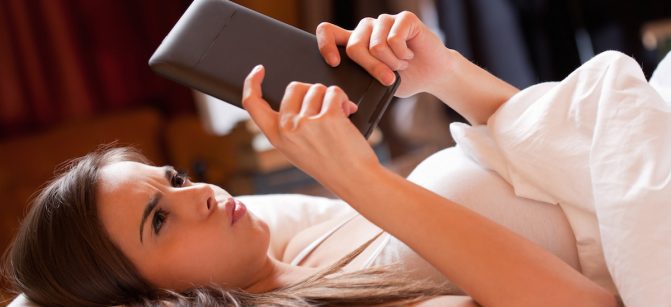 Cute young brunette  using tablet computer laying in bed.