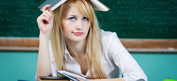 Closeup portrait annoyed, bored, tired, woman, funny looking student with book on head, sitting at desk, fed up of studying, isolated green chalkboard background. Face expression, emotion, reaction