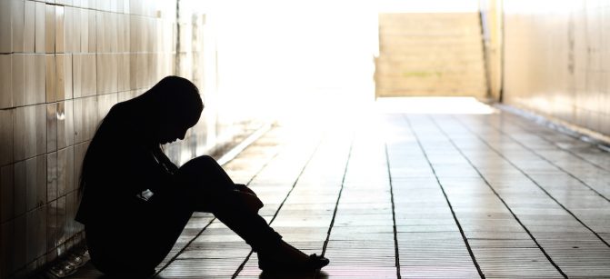 Backlight of a teenager depressed sitting inside a dirty tunnel