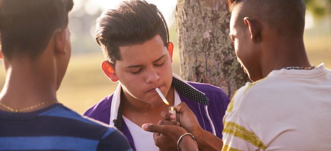 Youth culture, young people, group of male friends, mixed race teen outdoor, teenager in park. Hispanic kid smoking cigarette, confident boy, smoker. Health problems, social issues. Cigarettes