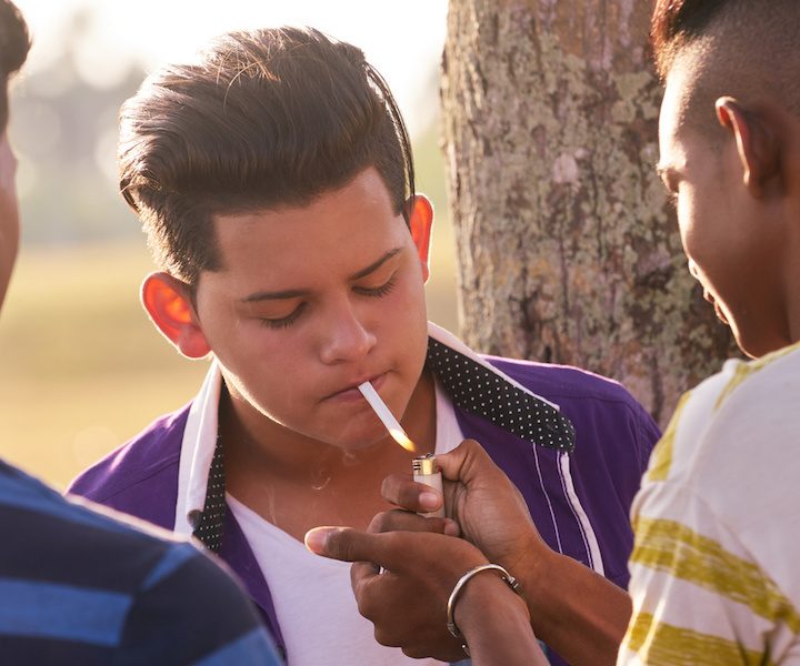 Youth culture, young people, group of male friends, mixed race teen outdoor, teenager in park. Hispanic kid smoking cigarette, confident boy, smoker. Health problems, social issues. Cigarettes