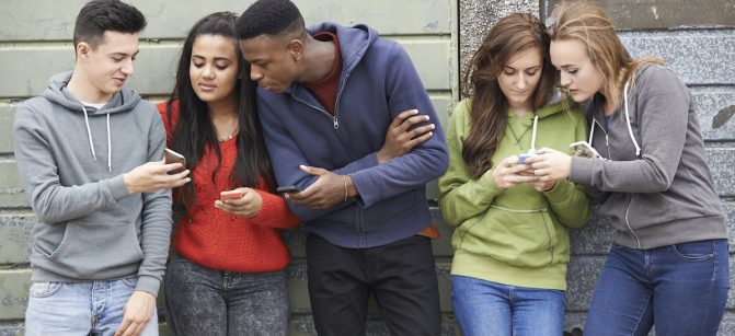 Group Of Teenagers Sharing Text Message On Mobile Phones