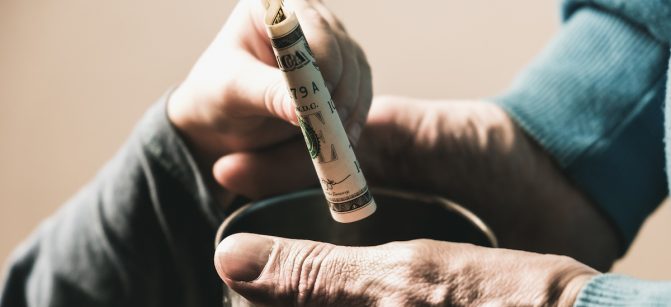 Close-up hands with cup Dirty hands of a beggar homeless man and a dollar bill of alms and help.