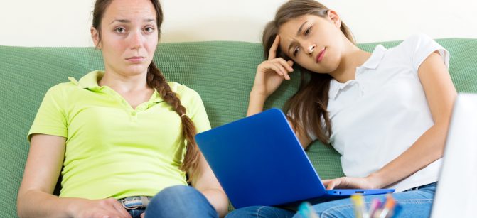 Two sad student sitting on the couch and working on laptop computers. Focus on the left woman