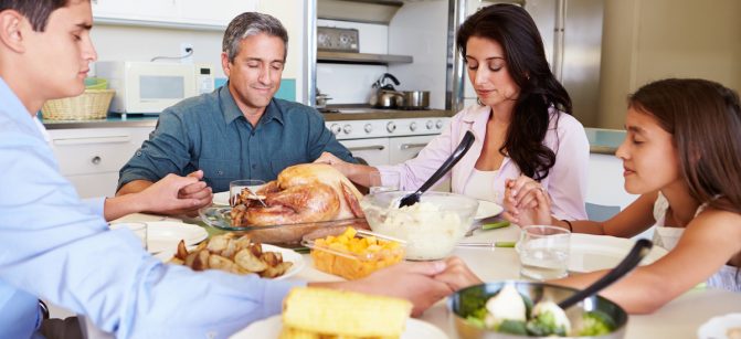 Family Sitting Around Table Saying Prayer Before Eating dinner