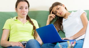 Two sad student sitting on the couch and working on laptop computers. Focus on the left woman
