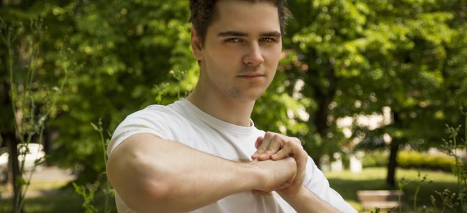 Attractive confident young man in nature environment holding fist with other hand