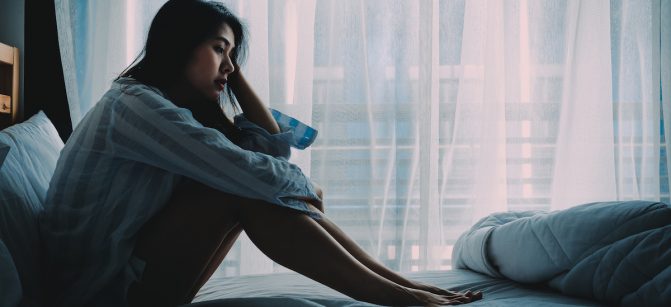 Unhappy beautiful Asian woman sitting on a bed looking sad and lonely