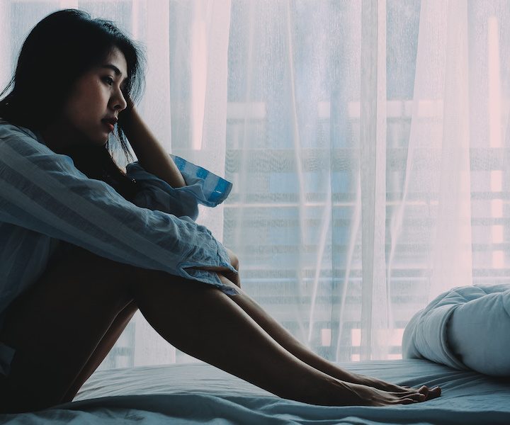 Unhappy beautiful Asian woman sitting on a bed looking sad and lonely