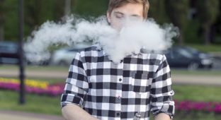 A young man smokes an electronic cigarette and uses a gyroscope.