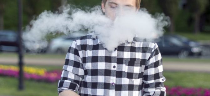 A young man smokes an electronic cigarette and uses a gyroscope.