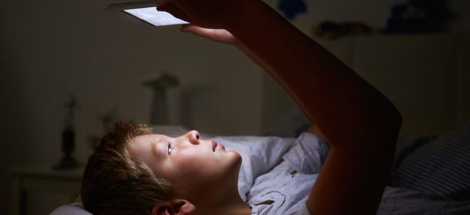 Boy Looking At Digital Tablet In Bed At Night