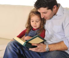 Father and sweet  little daughter reading book on couch together
