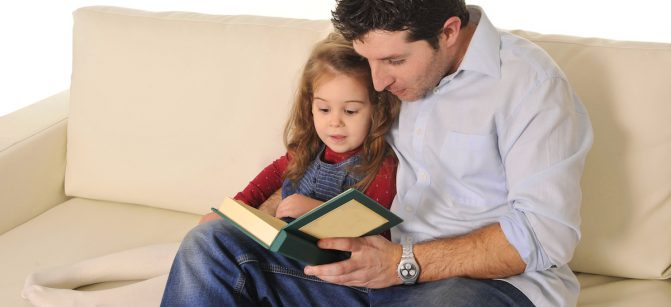 Father and sweet  little daughter reading book on couch together