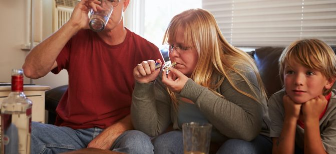 Parents Sit On Sofa With Children Taking Drugs And Drinking