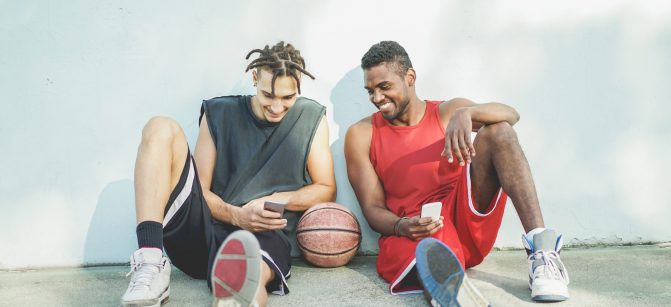 Young cheerful basket ball players having fun with smart phone outdoor - Best sport friends sharing free time with new trends technology - Technology and sporty lifestyle concept - Warm retro filter