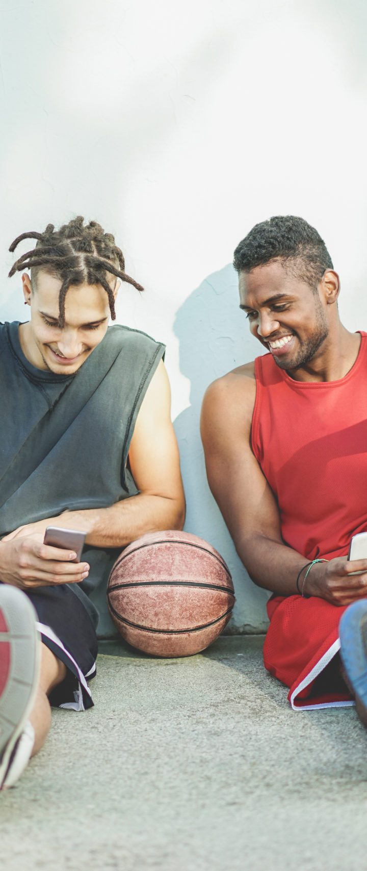 Young cheerful basket ball players having fun with smart phone outdoor - Best sport friends sharing free time with new trends technology - Technology and sporty lifestyle concept - Warm retro filter