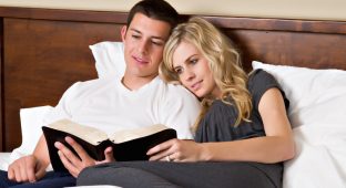 An attractive young couple read the Bible in bed