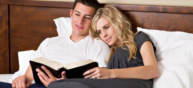 An attractive young couple read the Bible in bed