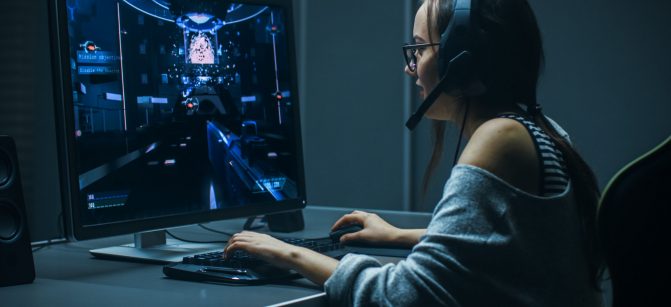 Beautiful Professional Gamer Girl Playing in First-Person Shooter Online Video Game on Her Personal Computer. Casual Cute Geek Girl Wearing Headset. In the Underground Gaming Club.