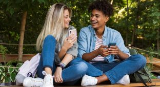 Image of excited emotional young loving couple using mobile phone outdoors in park.