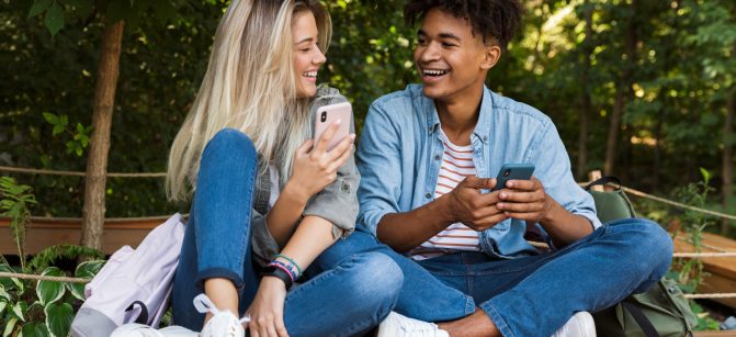 Image of excited emotional young loving couple using mobile phone outdoors in park.