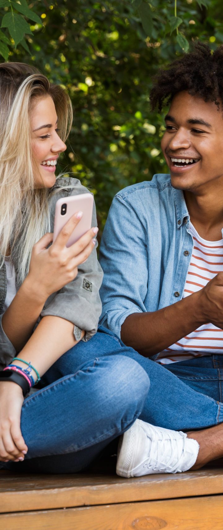 Image of excited emotional young loving couple using mobile phone outdoors in park.
