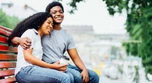Young african american couple in love hugging, kissing and sitting on the red bench in summer time. Love, holiday, travel and relationship concept