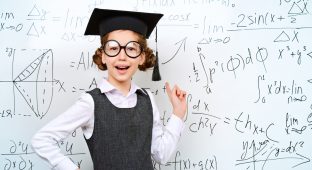 Happy smart schoolgirl in big glasses and academic hat performs the task at the blackboard. Education.