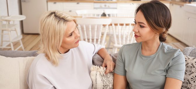 People, lifestyle, family, love and relationships concept. Indoor shot of blonde mature mother sitting on sofa with her young brunette daughter, talking, spending nice time together, drining tea