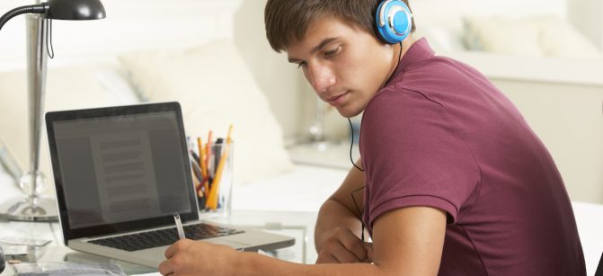 Teenage Boy Studying At Desk In Bedroom Wearing Headphones