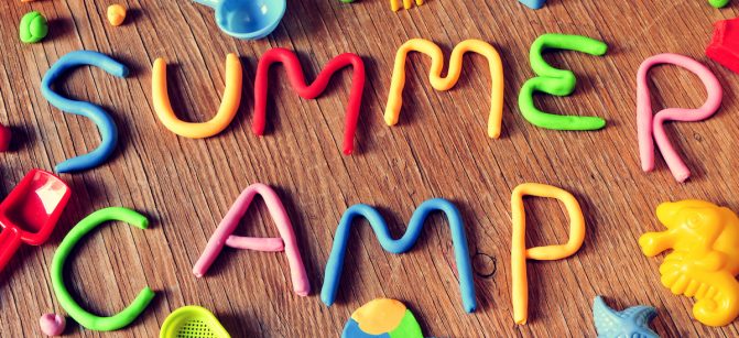 the text summer camp made from modelling clay of different colors and some beach toys such as toy shovels and sand moulds, on a rustic wooden surface