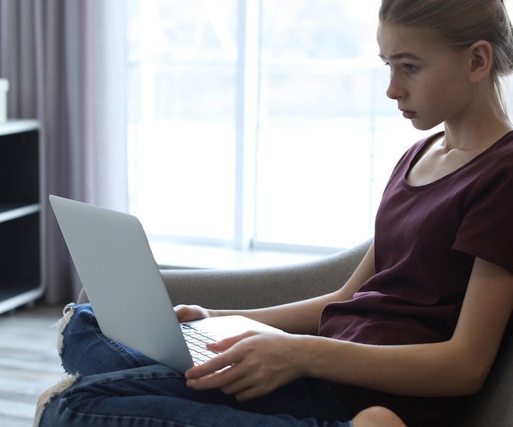 Shocked teenage girl with laptop in room. Danger of internet